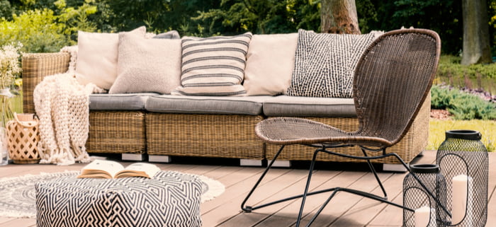 Patterned pouf and rattan chair on cozy wooden patio or deck with cushions and pillows on sofa and lanterns