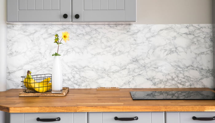 Modern minimal gray color kitchen with self adhesive fake marble imitation tape on wall, solid natural wood countertop with built in small stove and a banana an flower base on the side
