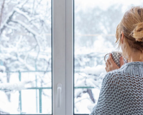 A woman looking out of the window at the snow-covered outdoors